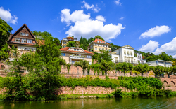 Häuser am Ufer eines Flusses bei sonnigem Wetter mit blauem Himmel und Wolken.