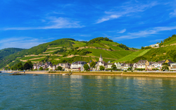 Flusslandschaft mit grünen Hügeln und kleinen Häusern am Ufer.