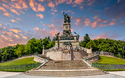 Monument auf Treppen mit Bäumen und farbigem Himmel im Hintergrund.