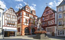 Fachwerkhäuser an einem Platz mit Brunnen und blauem Himmel.