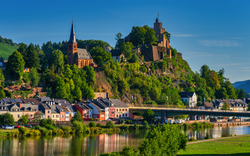 Burg und Kirche auf einem Hügel über einem Fluss mit Brücke und Häusern.