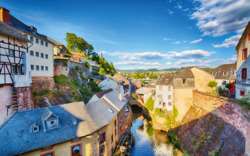 Malerische Altstadt mit Fluss und historischen Häusern bei sonnigem Wetter.