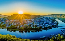 Sonnenaufgang über einer Flusslandschaft mit Stadt und umgebenden Hügeln.