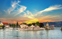Hafen von Lindau am Bodensee mit Boot, Leuchtturm und Stadtansicht bei Sonnenuntergang.