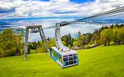 Seilbahn über grüne Wiese mit Blick auf See und Berge im Hintergrund