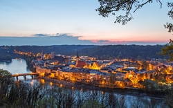 Stadtansicht bei Dämmerung mit Fluss und beleuchteten Gebäuden.