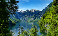 Bergsee mit umgebenden grünen Bergen und blauem Himmel im Hintergrund.
