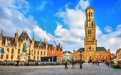 Historische Gebäude und Belfried auf einem Platz bei klarem Himmel.
