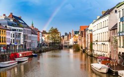 Kanal mit Booten und Regenbogen über einer Stadt mit historischen Gebäuden.