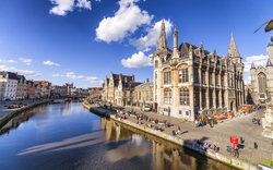 Blick auf die Stadt Gent in Belgien mit der Sint-Niklaaskerk und dem Fluss Leie bei sonnigem Wetter.