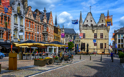 Historischer Platz mit bunten Gebäuden und Straßencafé unter blauem Himmel.