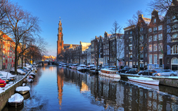 Kanal in Amsterdam mit Schneelandschaft und Kirchturm im Hintergrund.