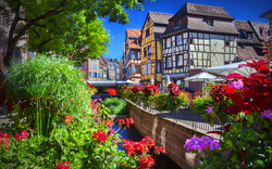 Fachwerkhäuser und Blumen entlang eines kleinen Kanals an einem sonnigen Tag.
