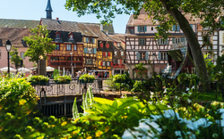 Fachwerkhäuser an einem sonnigen Tag im historischen Stadtzentrum mit Brücke und Blumen.