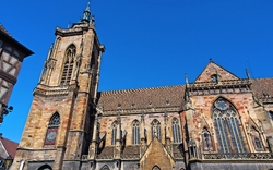 Gotische Kirche mit großem Turm und bunten Fenstern vor blauem Himmel.