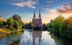 Kirche mit zwei Türmen an einem Fluss bei Sonnenuntergang.