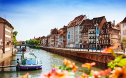 Kanalufer mit Fachwerkhäusern und Boot in Straßburg bei sonnigem Wetter.