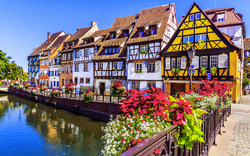 Fachwerkhäuser an einem Kanal mit Blumen geschmückter Brücke.