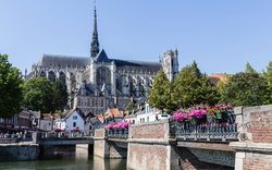 Gotische Kathedrale mit Brücke, Fluss und bepflanzten Blumen in einer Stadtumgebung.