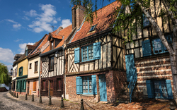 Fachwerkhäuser mit bunten Fenstern an einer Kopfsteinpflasterstraße bei sonnigem Wetter.