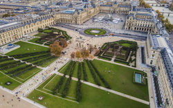 Luftaufnahme des Louvre-Museums in Paris mit großen Gartenanlagen und dem Gebäude im Hintergrund.