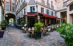 Straßenrestaurant mit roten Markisen und Tischen auf Kopfsteinpflasterstraße.