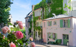 Straßenszene mit pastellfarbenen Häusern und blühenden Rosen im Vordergrund.