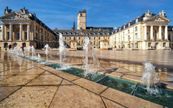 Platz mit Brunnen vor historischem Gebäude bei sonnigem Wetter.