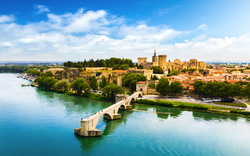 Stadtansicht mit alter Brücke über einem Fluss und historischem Gebäude im Hintergrund.