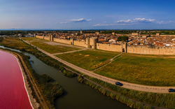 Luftaufnahme einer befestigten Stadt neben einem pinken See und einer Straße.