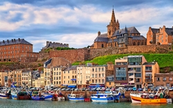Hafen mit bunten Fischerbooten vor historischem Stadtpanorama und Kirche im Hintergrund.