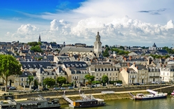 Stadtansicht mit Fluss, alten Gebäuden und Kirchturm unter blauem Himmel.