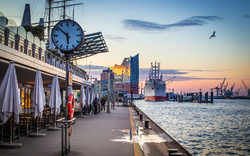 Hafenpromenade bei Sonnenuntergang mit Schiff und Elbphilharmonie im Hintergrund.