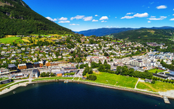 Luftaufnahme einer Stadt mit Wasser und grünen Hügeln im Hintergrund.