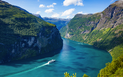 Fjord mit grünen Berghängen und einem weißen Kreuzfahrtschiff auf blauem Wasser.