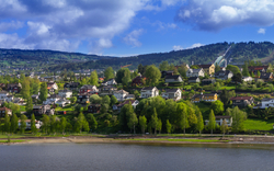 Kleinstadt am See mit Hügeln und bewölktem Himmel im Hintergrund.