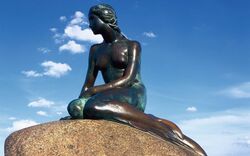 Bronzestatue der kleinen Meerjungfrau auf einem Felsen vor blauem Himmel.