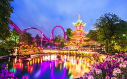 Vergnügungspark mit beleuchtetem Gebäude und Achterbahn am Abend.