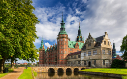 Historisches Gebäude mit Türmen und Wassergraben bei sonnigem Wetter.