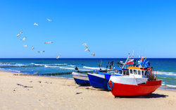 Boote am Sandstrand mit fliegenden Möwen und blauem Himmel.