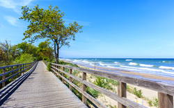 Holzsteg entlang des weißen Sandstrandes von Kolberg bei sonnigem Wetter mit Blick auf die Ostsee.
