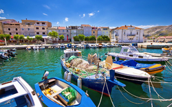 Boote im Hafen eines malerischen mediterranen Dorfes mit bunten Häusern im Hintergrund.