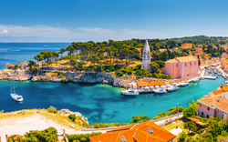 Küstenstadt mit Kirche am Meer, blaues Wasser und Boote, mediterrane Landschaft