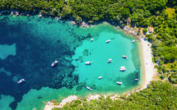 Luftaufnahme einer Bucht mit grünem Wald, klarem Wasser und Booten.