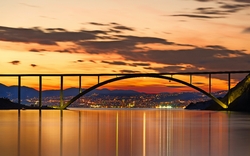 Brücke bei Sonnenuntergang mit Stadt und Bergen im Hintergrund.