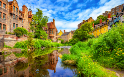 Historische Gebäude und Fluss in grüner Landschaft bei sonnigem Wetter.