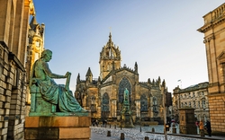 Statue vor einer historischen gotischen Kathedrale auf einem Platz, umgeben von alten Gebäuden.