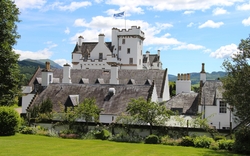 Weißes Schloss mit Flagge, umgeben von grüner Landschaft unter blauem Himmel.