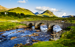 Steinbrücke über einen Fluss in einer bergigen Landschaft.