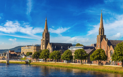 Fluss in einer Stadt mit Kirchen und Bäumen, blauer Himmel im Hintergrund.